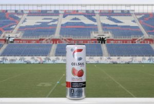 A strawberry and guava-flavored Celsius energy drink with the bleachers of the FAU Football Stadium in the background.