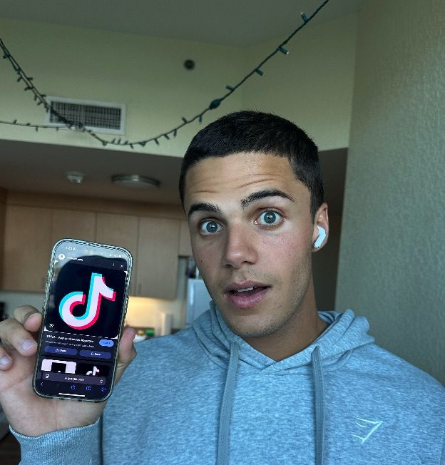 Photo of TikTok user and FAU student Tristin Trivers posing next to the TikTok app.