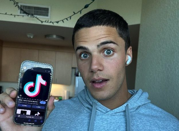 Photo of TikTok user and FAU student Tristin Trivers posing next to the TikTok app.